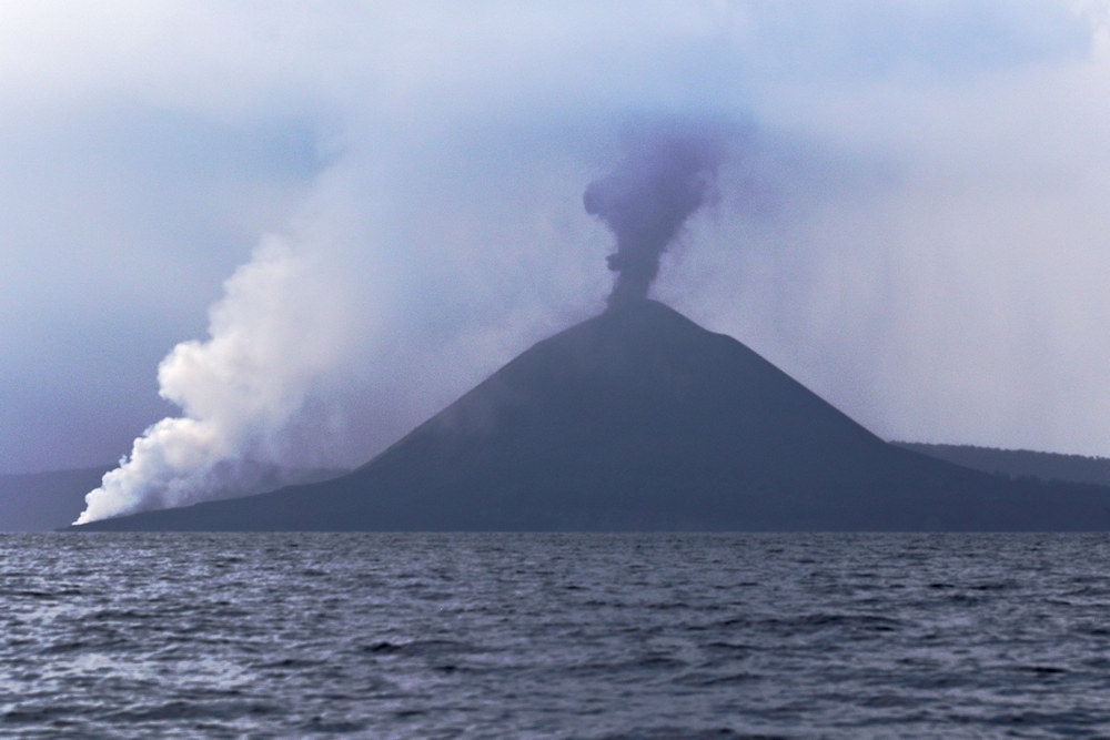 approaching broody Anak Krakatau - gently venting with lava flowing into sea generating steam (LHS)